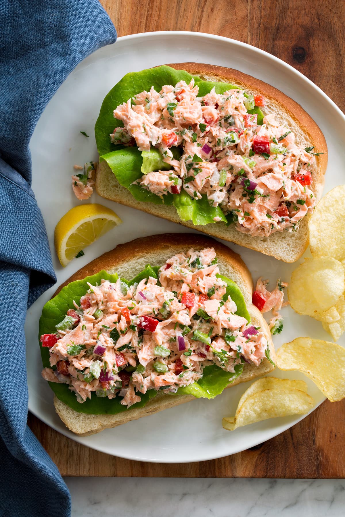 Salmon salad served over bread slices and lettuce leaves. Shown on a plate with potatoes chips and lemon slices to the side.