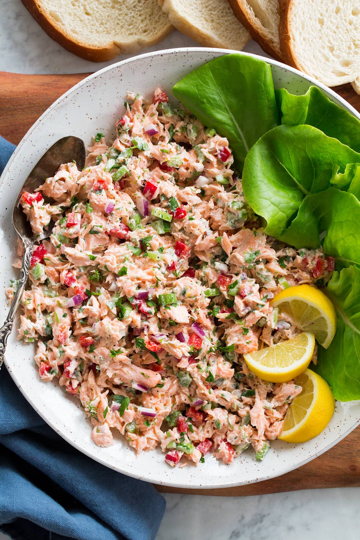 White bowl filled with salmon salad, lettuce leaves, lemon slices and a spoon to the side.