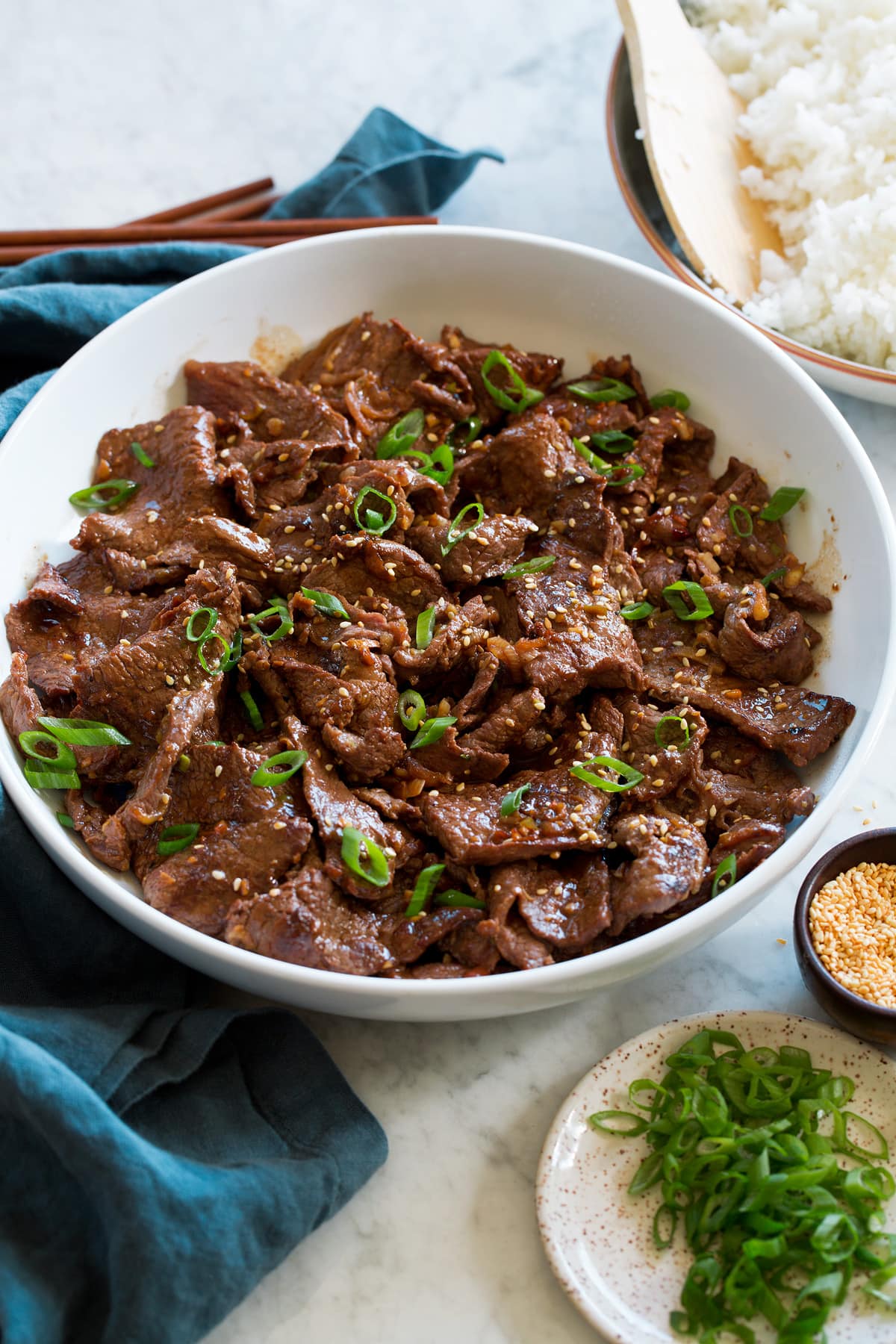 Bowl full of Korean bulgogi beef shown at a side angle on a marble surface.