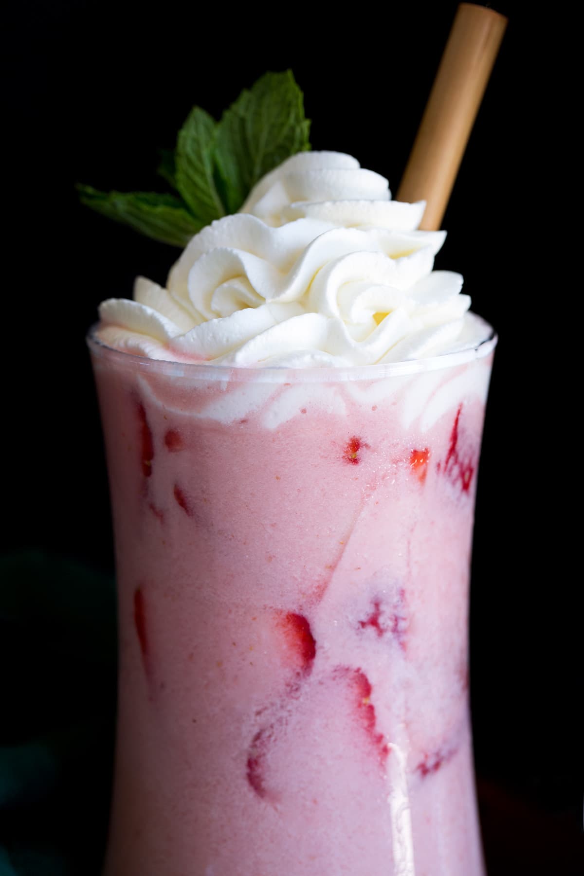 Close up photo of pink drink in a glass with a wooden straw.