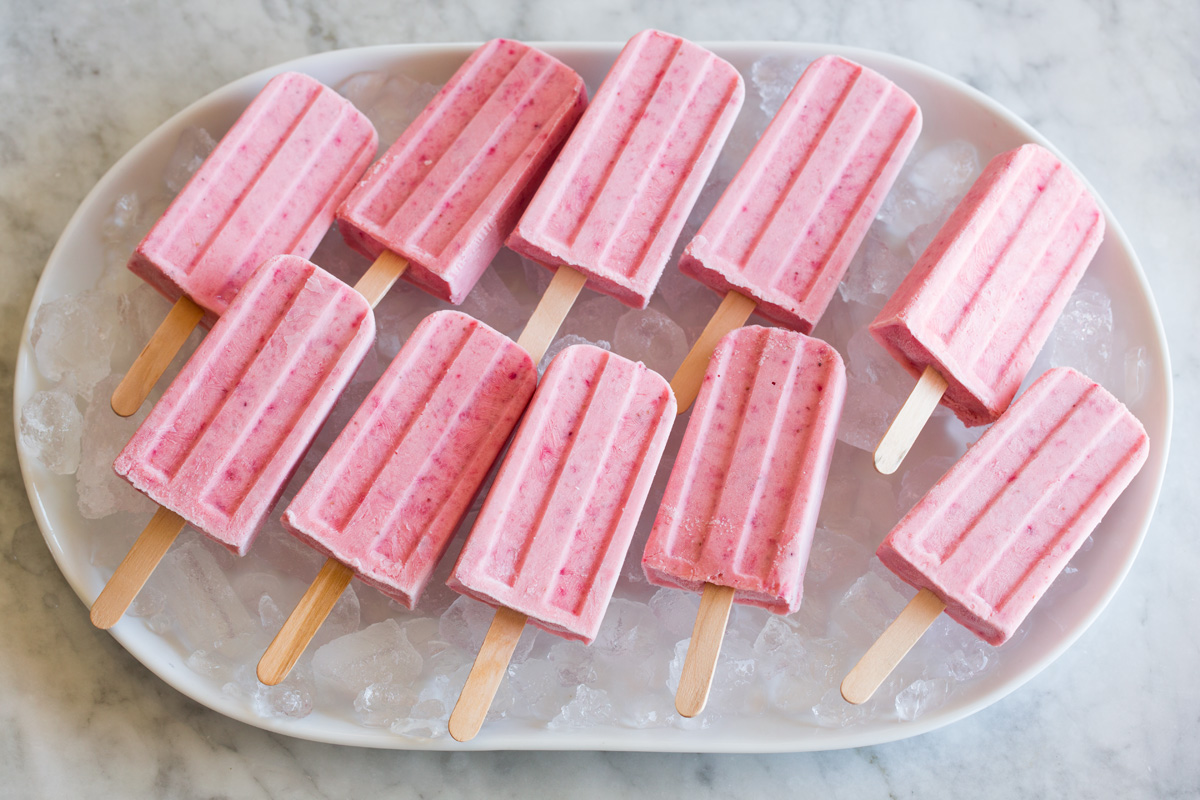 Strawberry popsicles on an oval platter with ice.