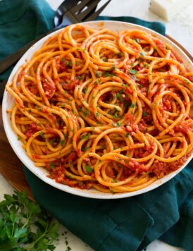 Bucatini with amatriciana sauce in a white serving bowl with parmesan cheese and parsley garnish.