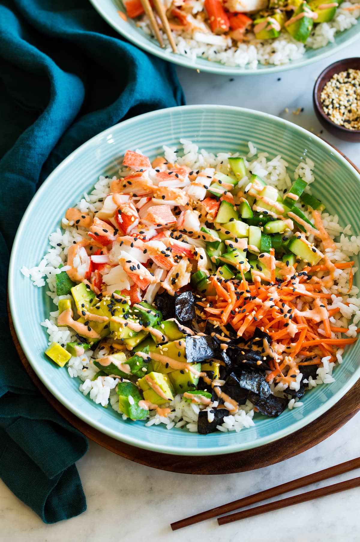 California roll sushi bowl shown in a blue bowl from a side angle. Bowl is resting on a wooden plate over a marble surface.