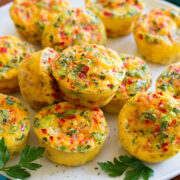 Egg muffins shown on a white serving platter over a wooden platter and a blue cloth.