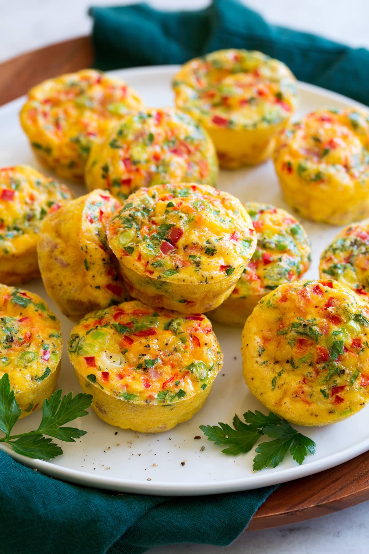 Egg muffins shown on a white serving platter over a wooden platter and a blue cloth.