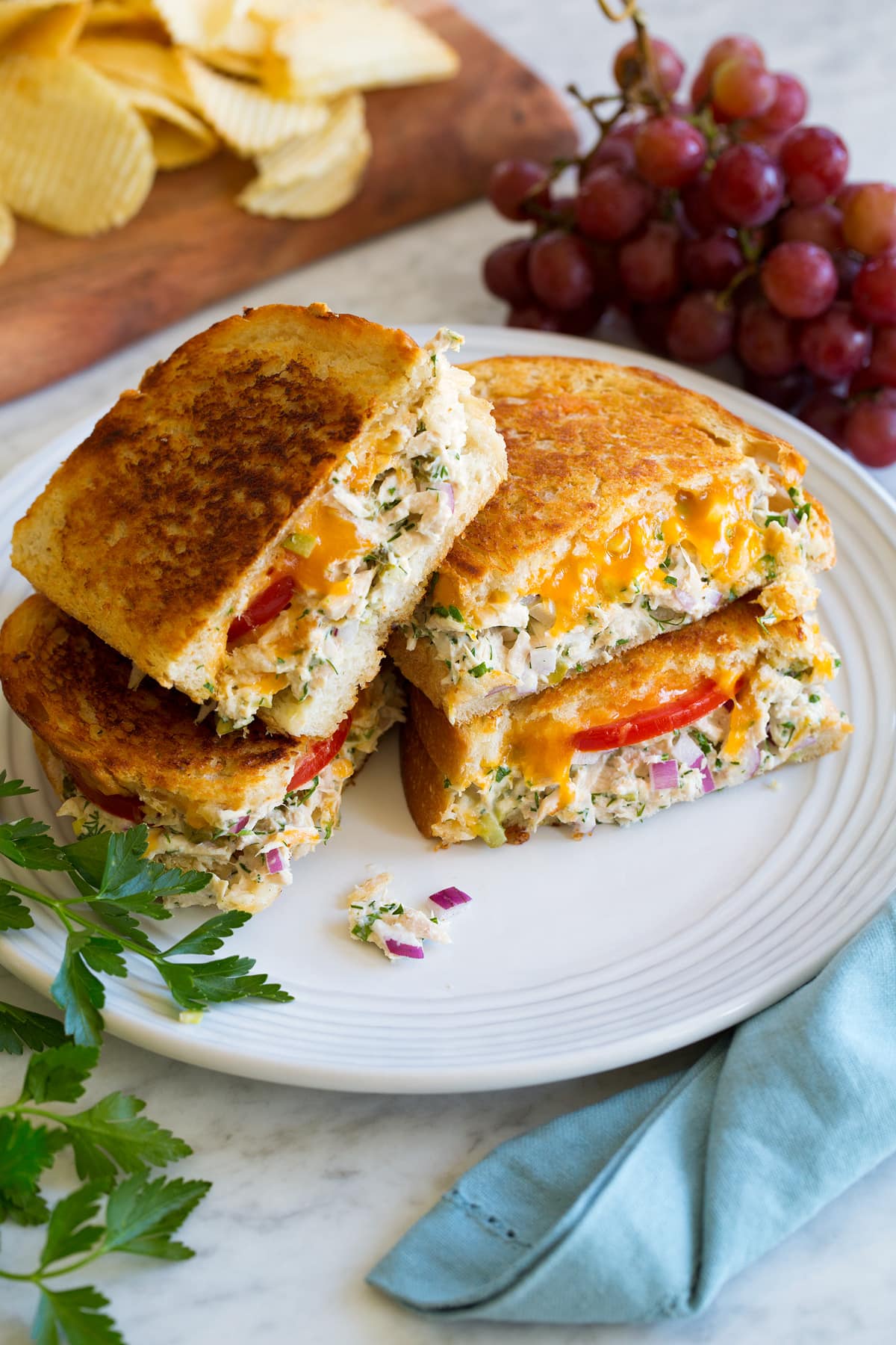 Two tuna melt sandwiches cut into halves and stacked on a large white plate.