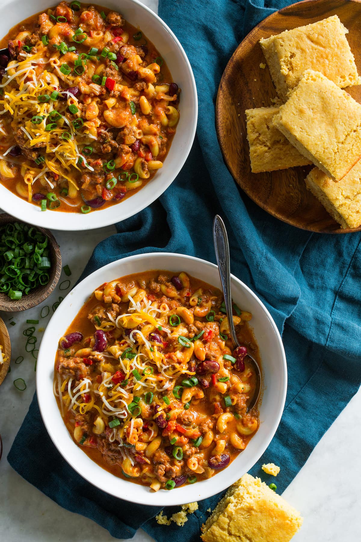 Two servings of chili mac shown in serving bowls from overhead. Cornbread slices are shown to the side as a serving suggestion.