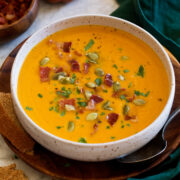 Single serving of pumpkin soup topped with bacon, parsley and pumpkin seeds.