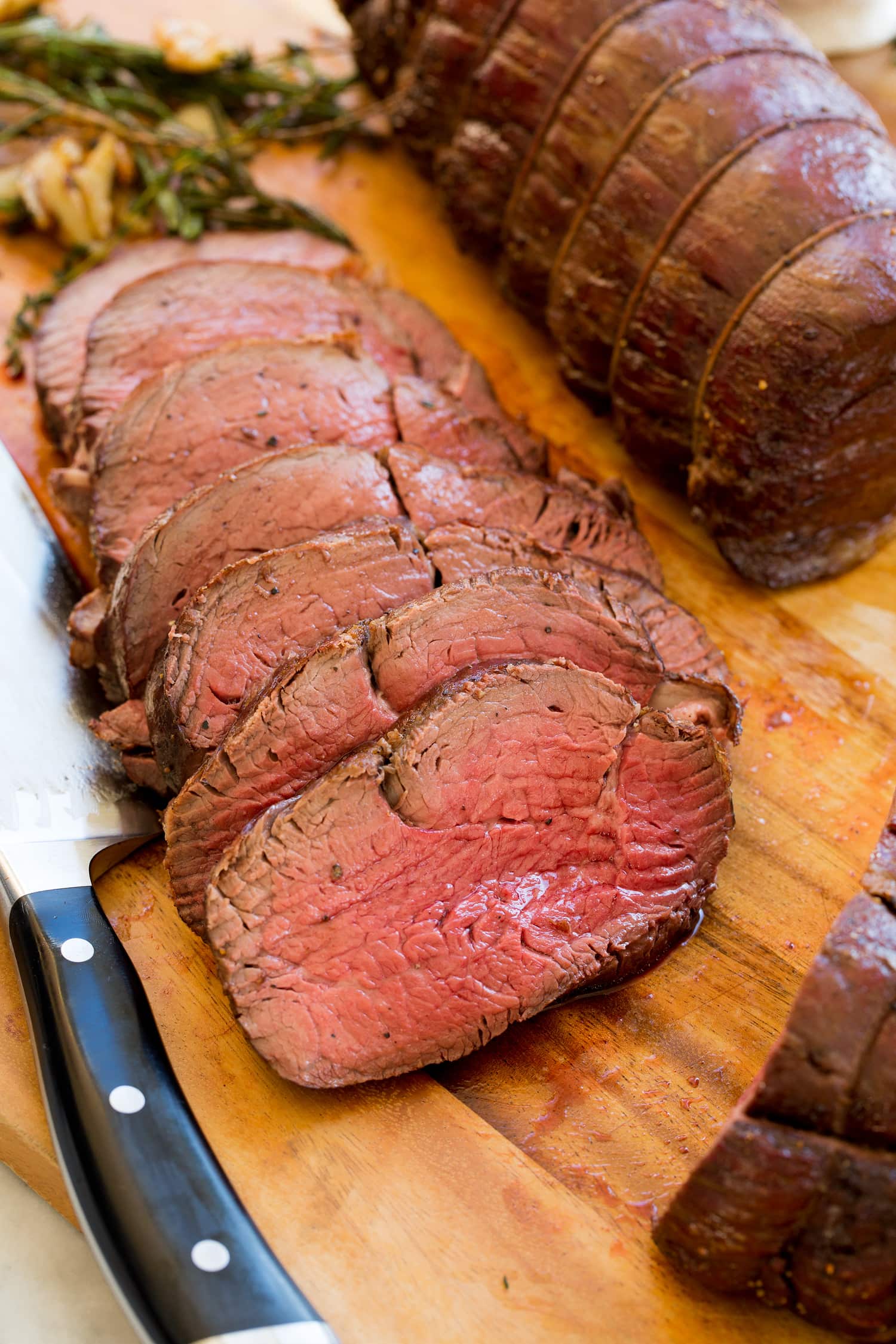 Beef tenderloin sliced on wood cutting board.