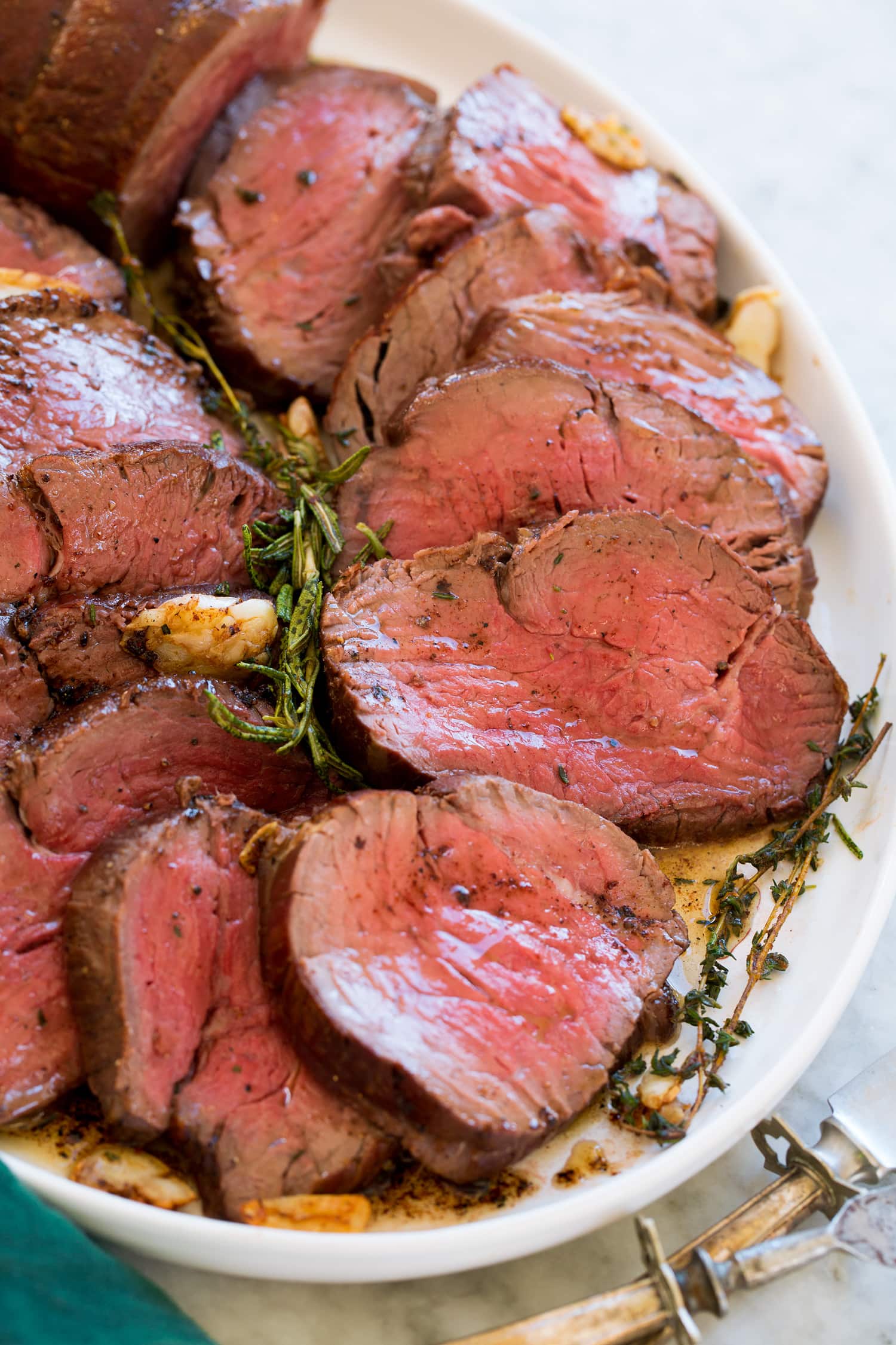 Close up photo of beef tenderloin cut into slices on a white serving platter.