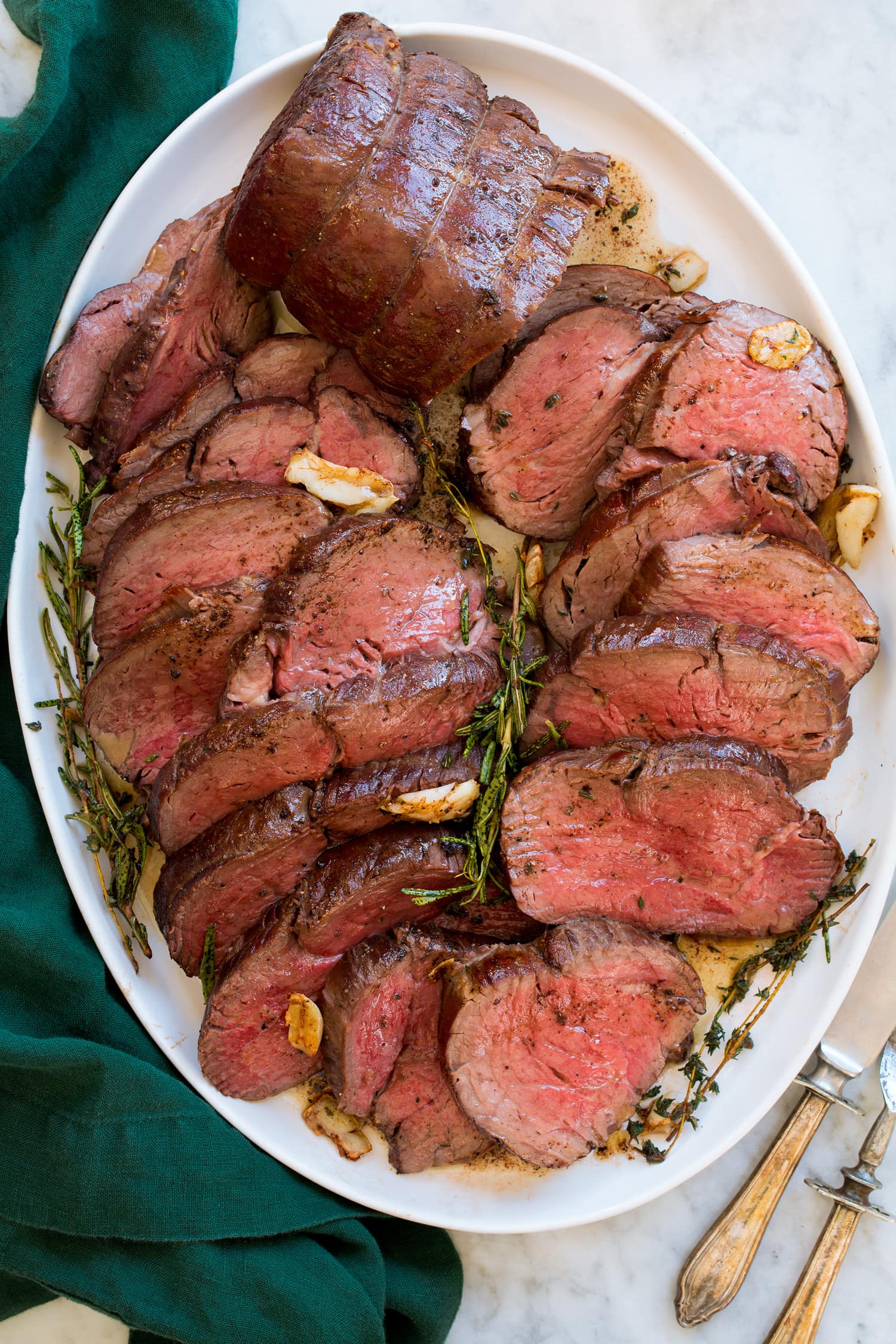 Beef Tenderloin arranged on a white oval platter shown from above on a white marble surface with a green cloth.