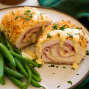 Chicken Cordon Bleu shown sliced in half with sauce on top. Green beans shown to the side.