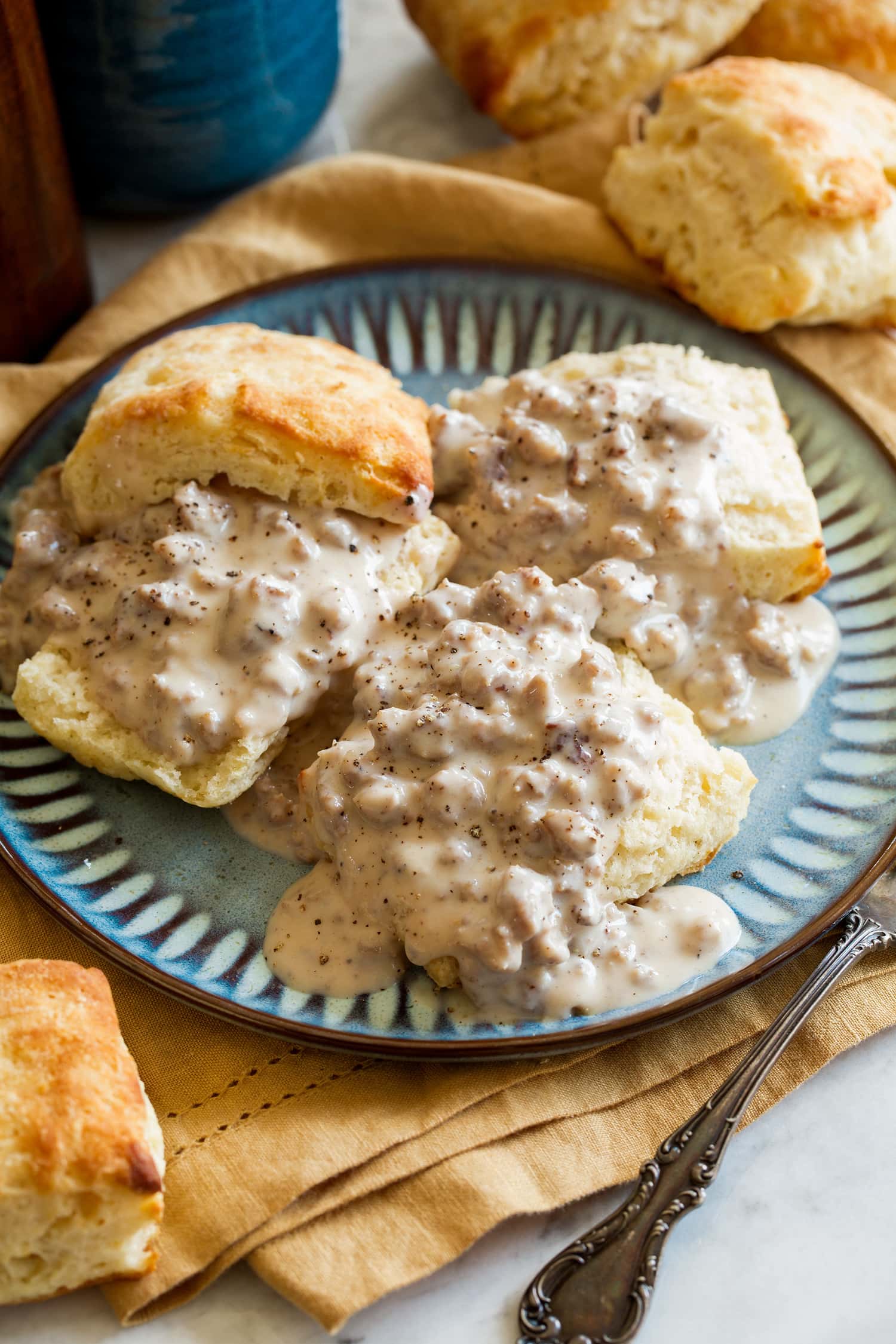 Three buttermilk biscuits with sausage gravy on a blue plate.