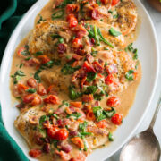 Creamy bacon tomato spinach chicken served on a white oval platter with a green cloth to the side.