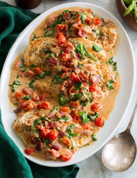 Creamy bacon tomato spinach chicken served on a white oval platter with a green cloth to the side.