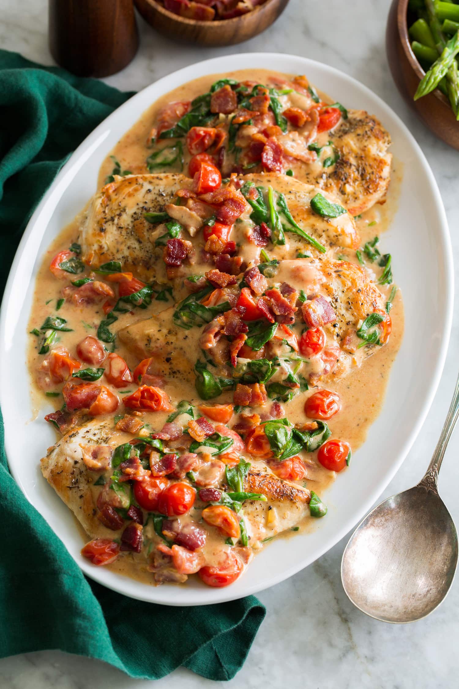 Creamy bacon tomato spinach chicken served on a white oval platter with a green cloth to the side.