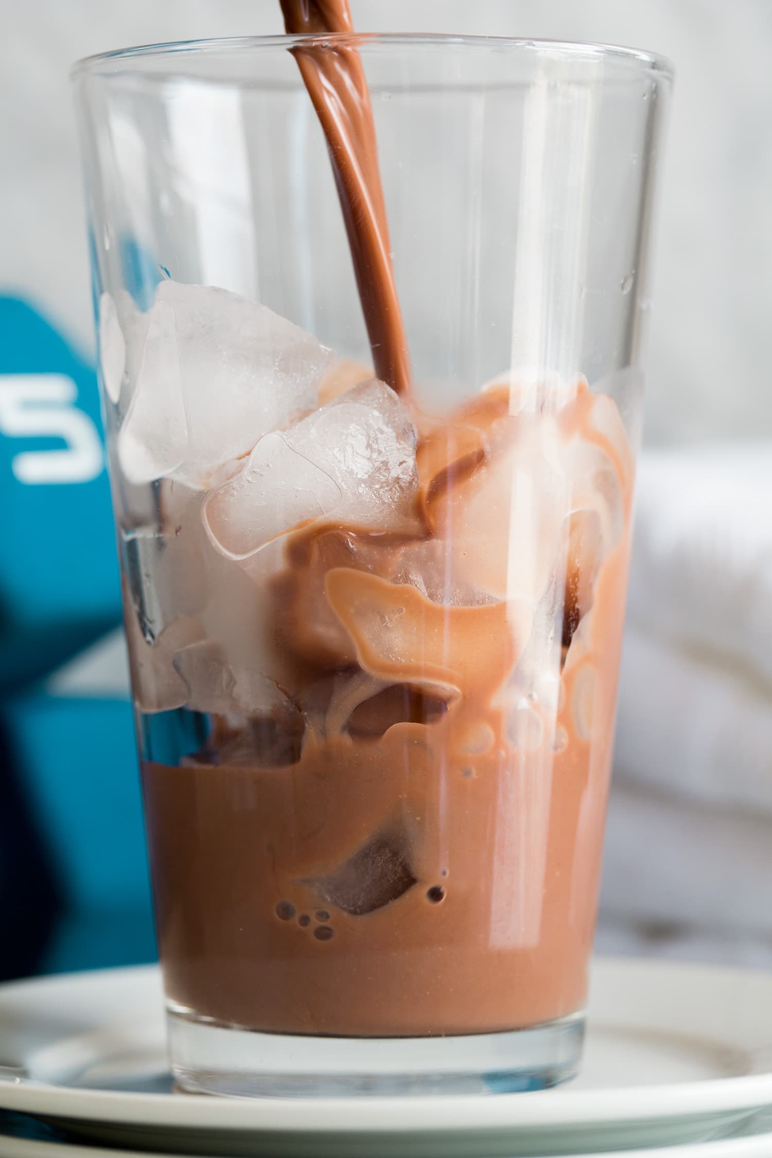 Chocolate peanut butter protein drink being poured over a glass cup of ice.