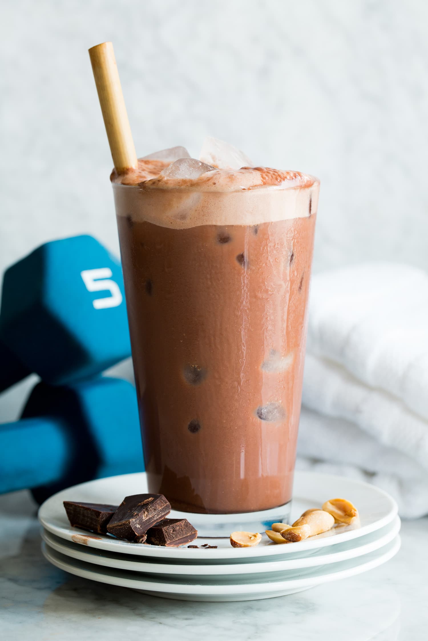 Homemade chocolate protein drink. Served on a stack of small plates with chocolate and peanuts to show flavor. Shown with weights in the back ground.