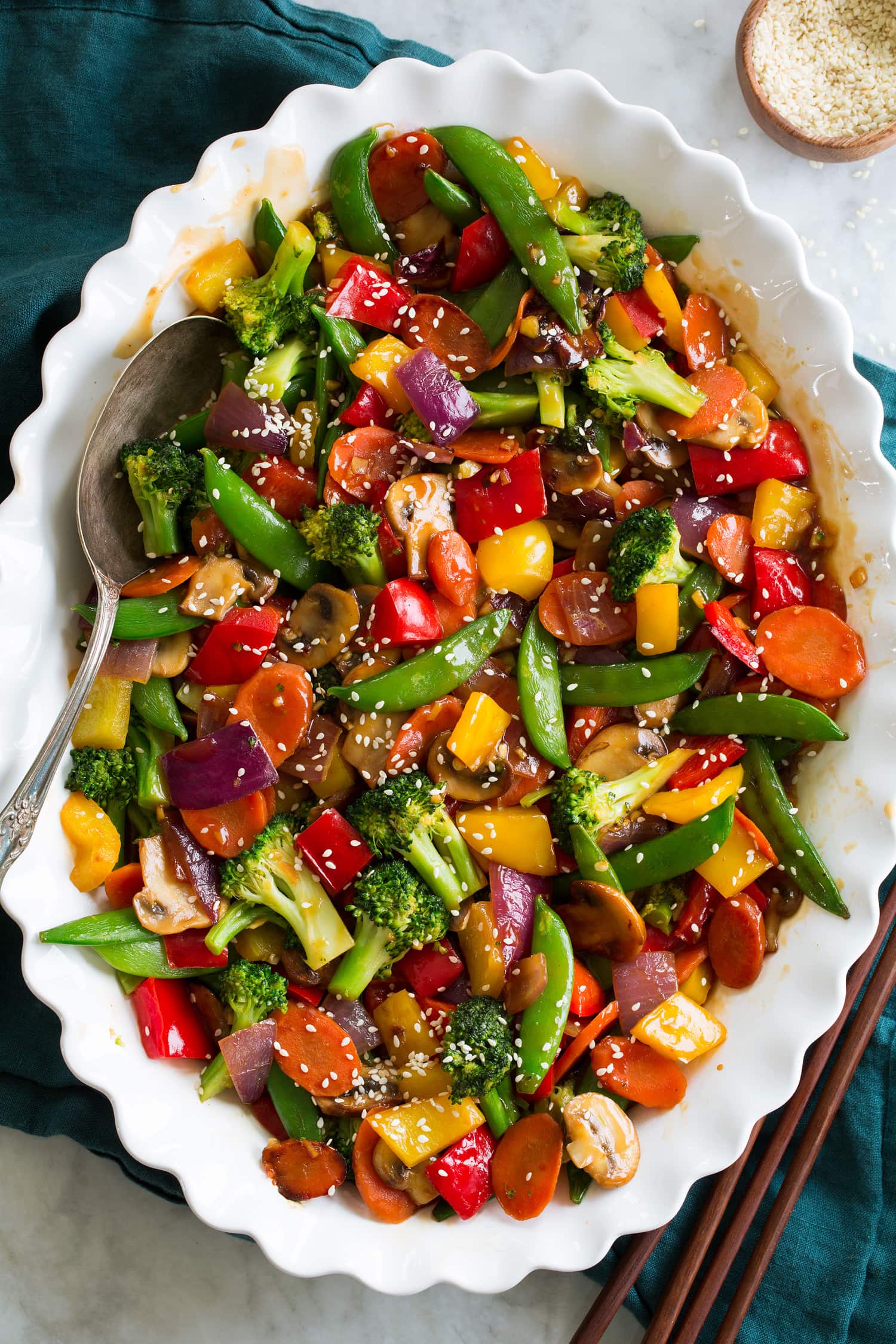 Vegetable stir fry in a white oval platter shown from above on a marble surface with a blue cloth.