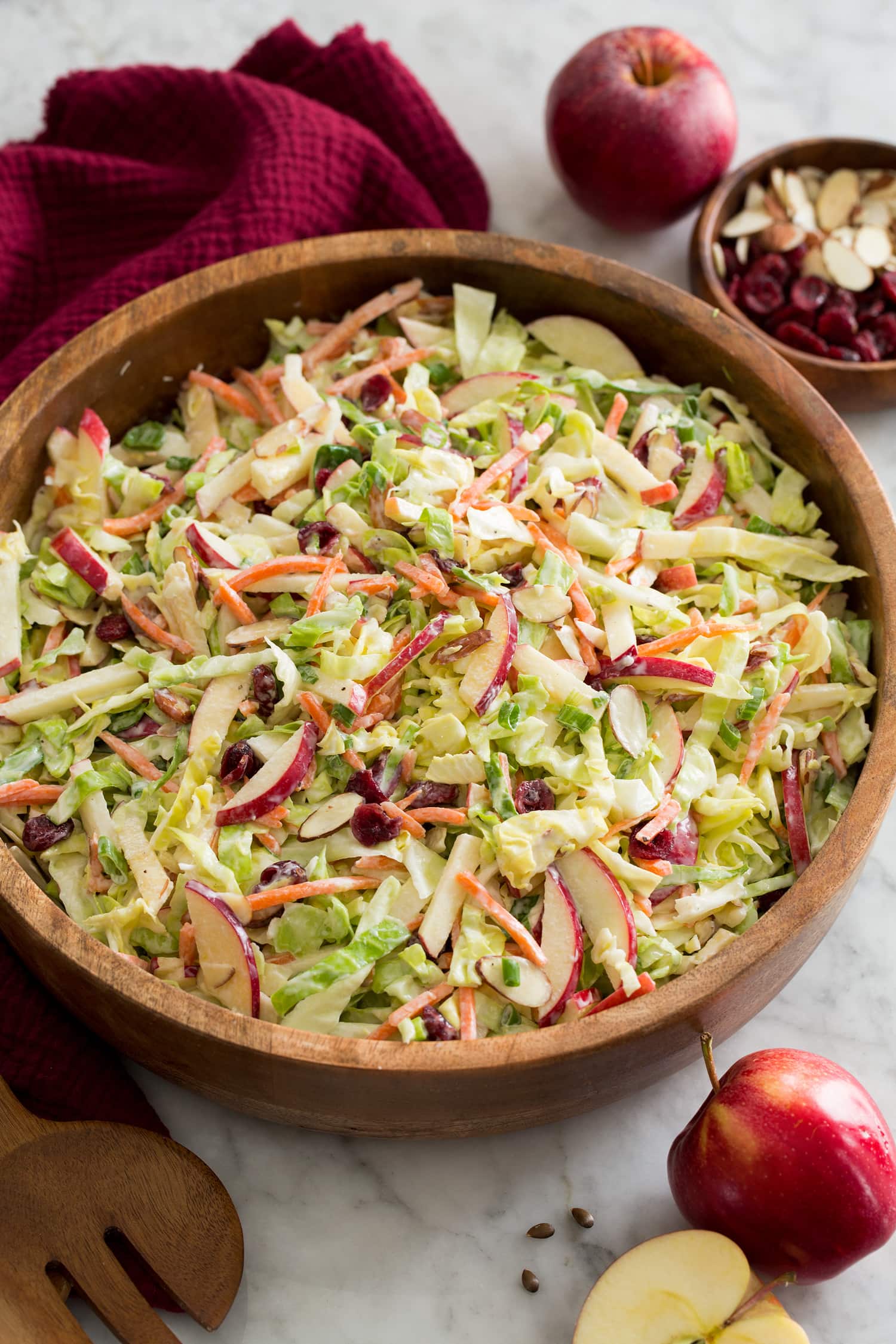 Homemade apple slaw with shredded cabbage, apples, carrots, almonds and dressing shown in a wooden salad bowl.