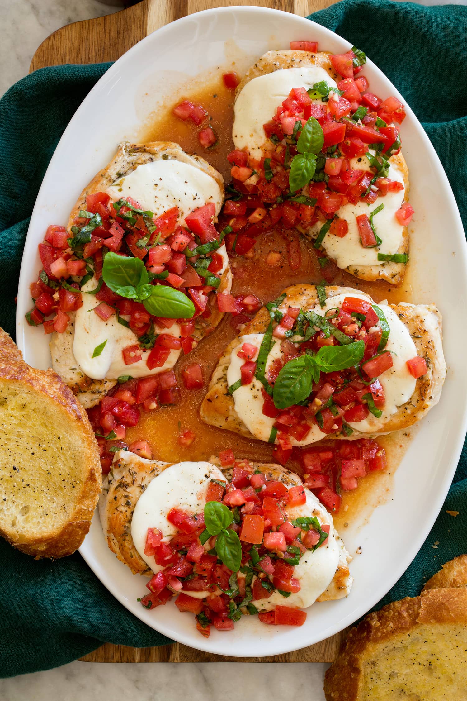 Overhead photo of four servings of bruschetta chicken on a white oval serving tray shown from above.