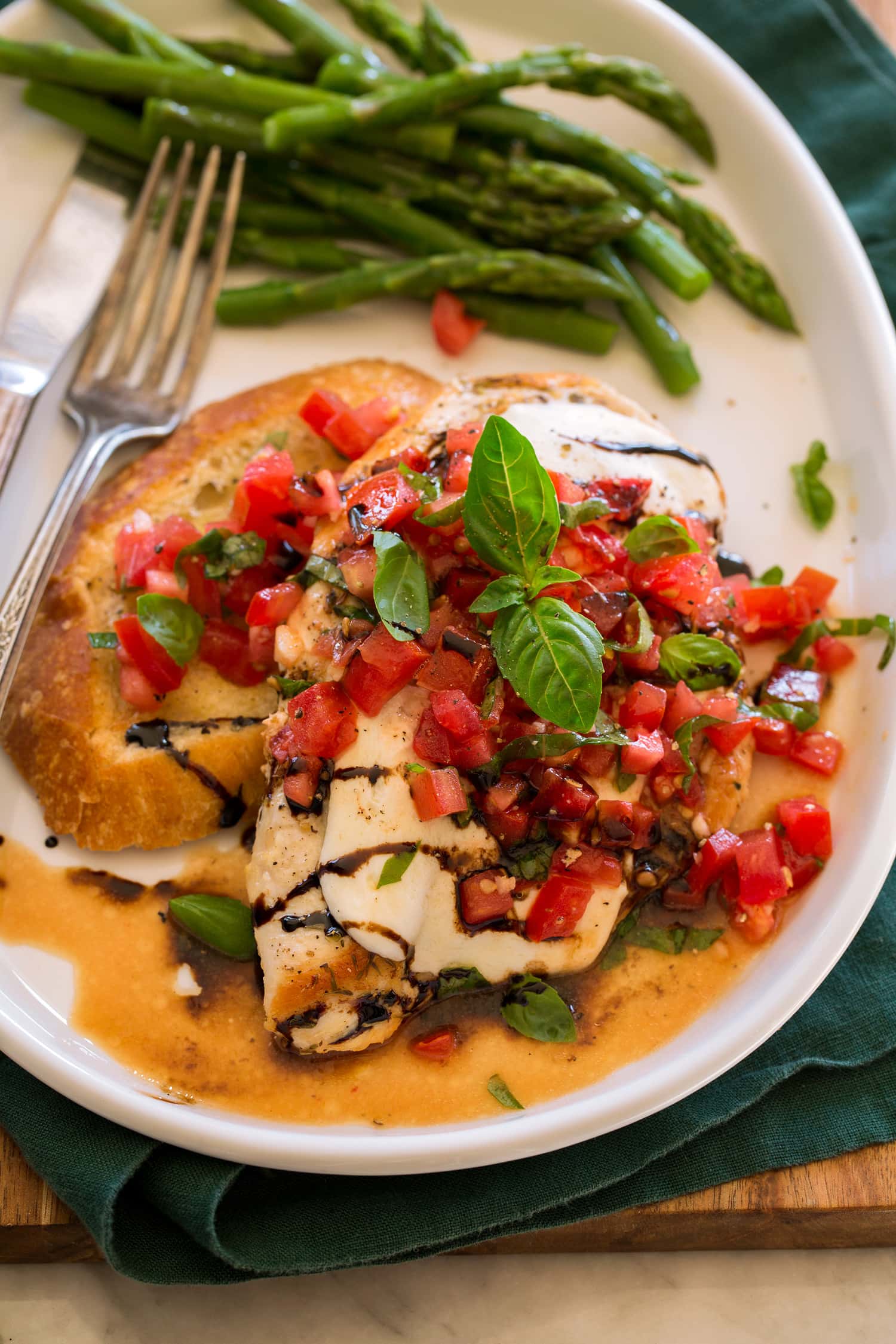 Bruschetta Chicken served with balsamic glaze and a side of toasted baguette and asparagus.