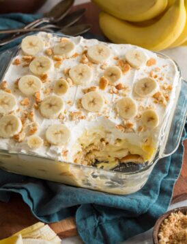 Banana pudding in glass square dish with scoop removed to show layers of the dessert.