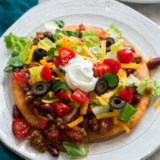 Homemade navajo taco on a plate. Made with homemade fry bread, ground beef and bean filling, lettuce, tomatoes, olives and sour cream.