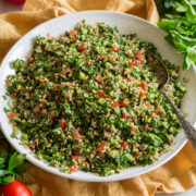 Herb tabbouleh shown in a white ceramic bowl over a yellow cloth.