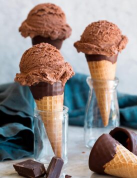 Three servings of chocolate ice cream on sugar cones.