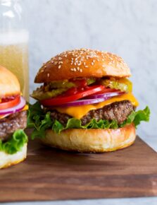 Hamburger shown on homemade bun with lettuce, cheddar, tomatoes and pickles.