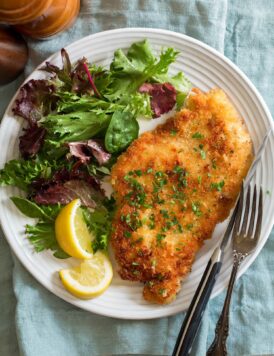 Chicken schnitzel shown served with lemons and a spring salad.