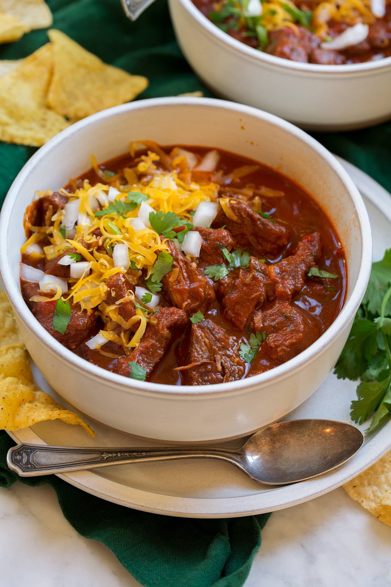 Chili con carne in a serving bowl topped with shredded cheese, cilantro and chopped onion.