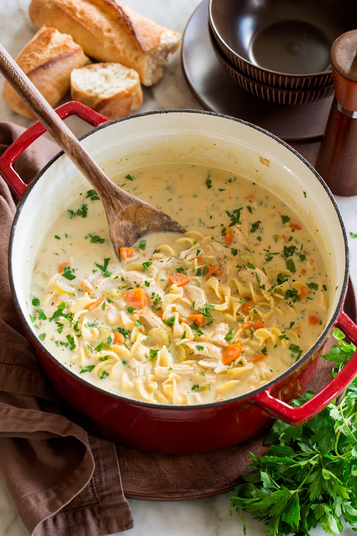 Pot full of homemade creamy chicken noodle soup served with a side of bread.