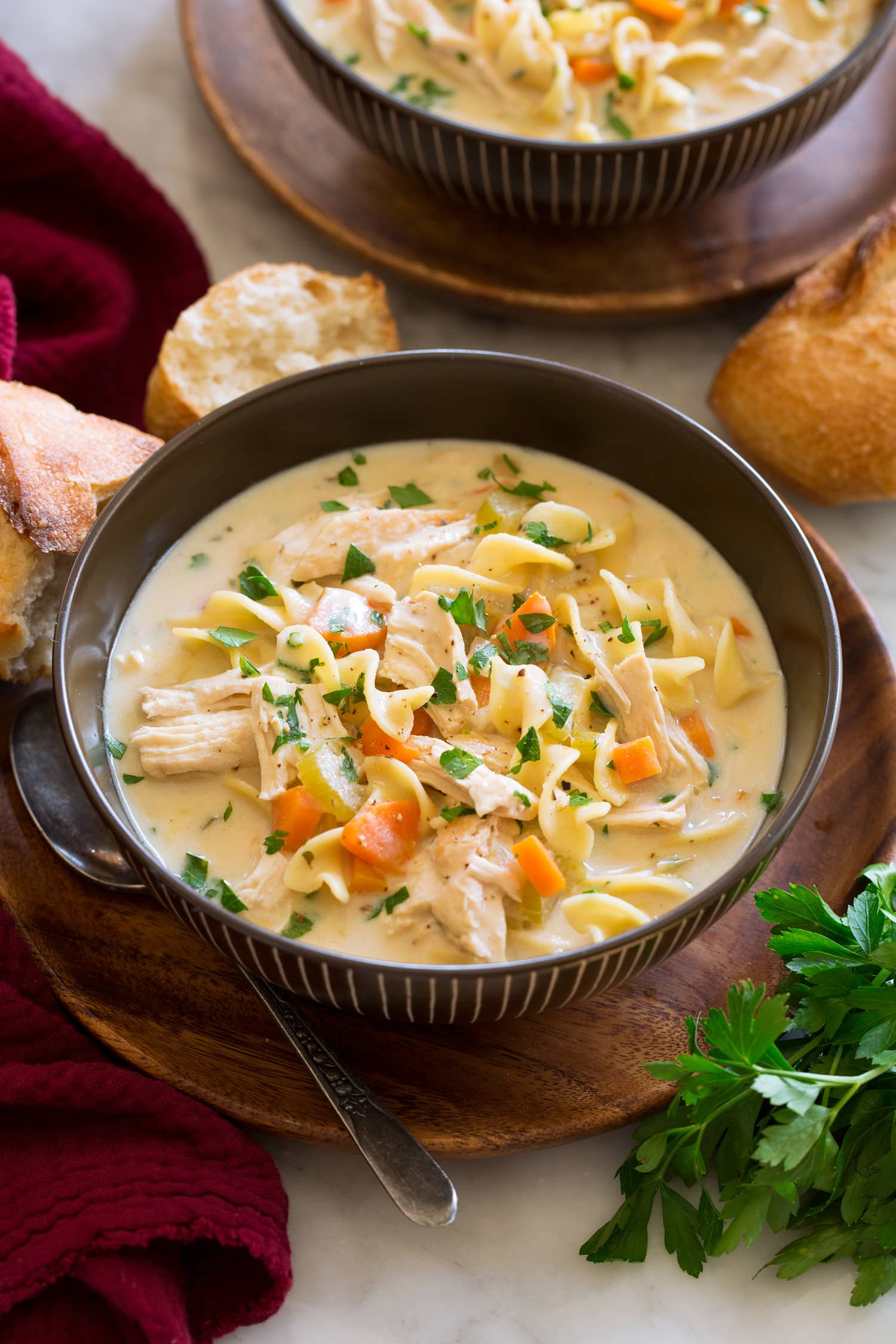 Serving of creamy chicken noodle soup shown in a brown bowl over a wooden plate.