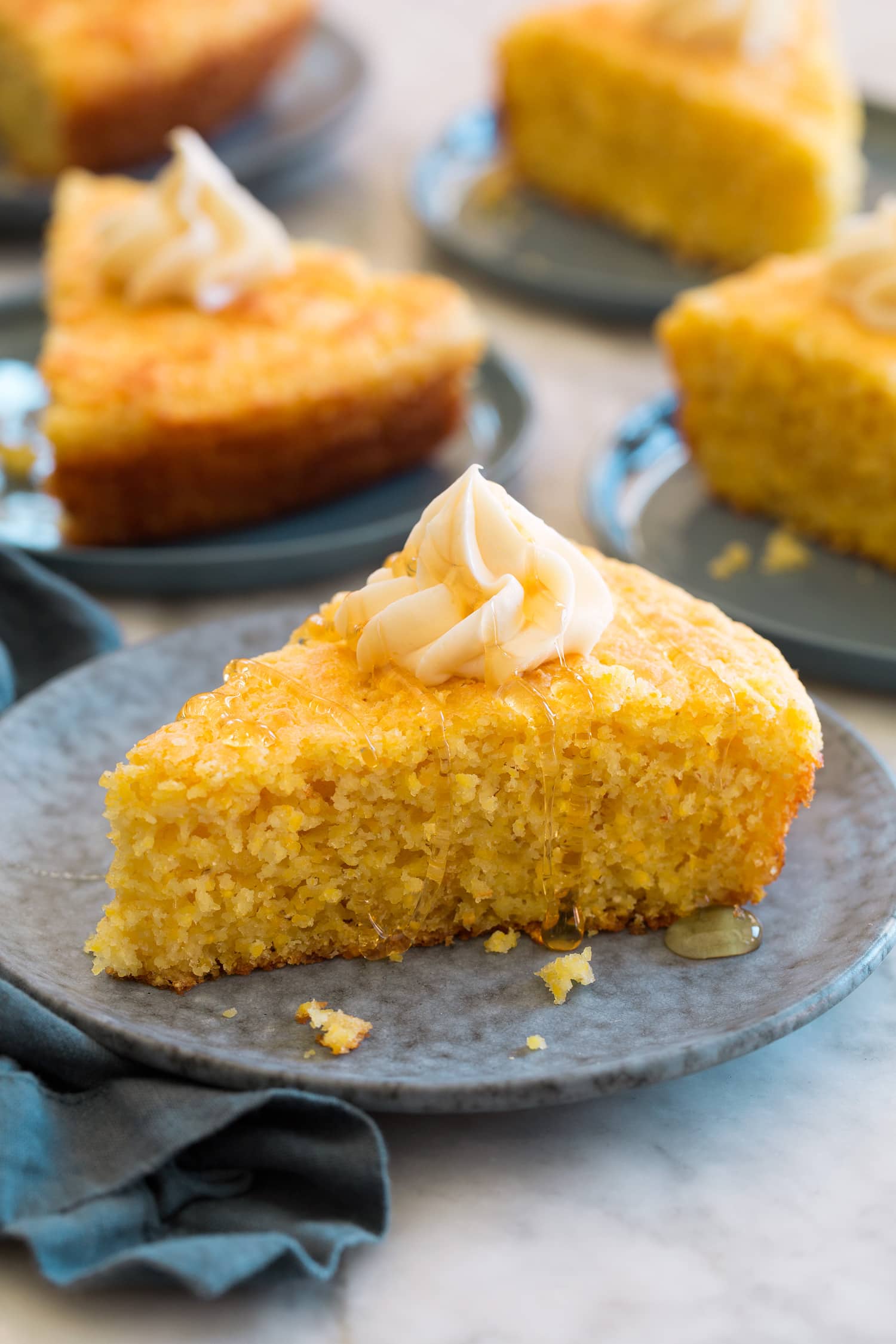 Slice of southern cornbread shown on a plate, it's topped with a swirl of honey butter.