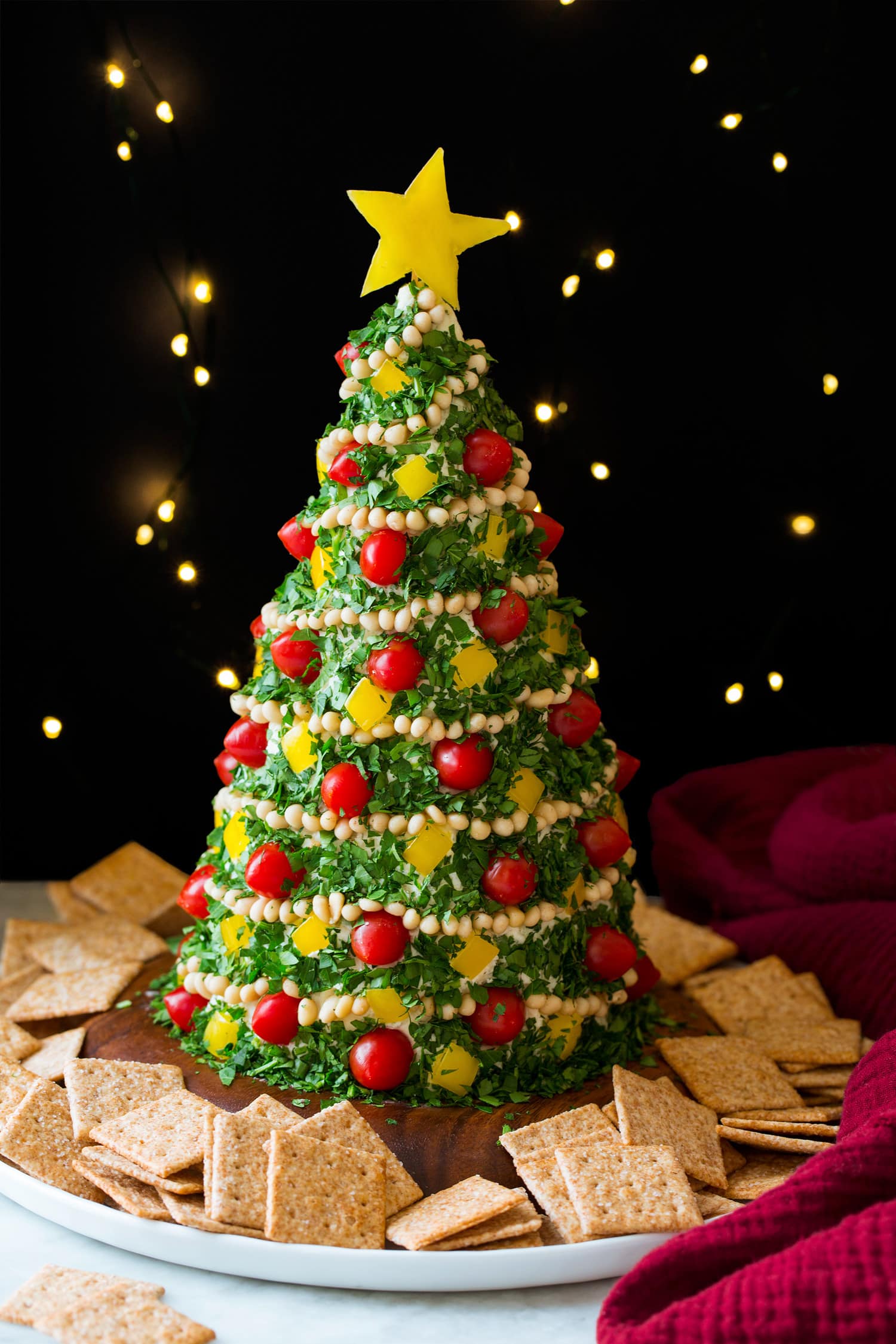 Christmas tree cheese ball with lights in the background and crackers around the tree.