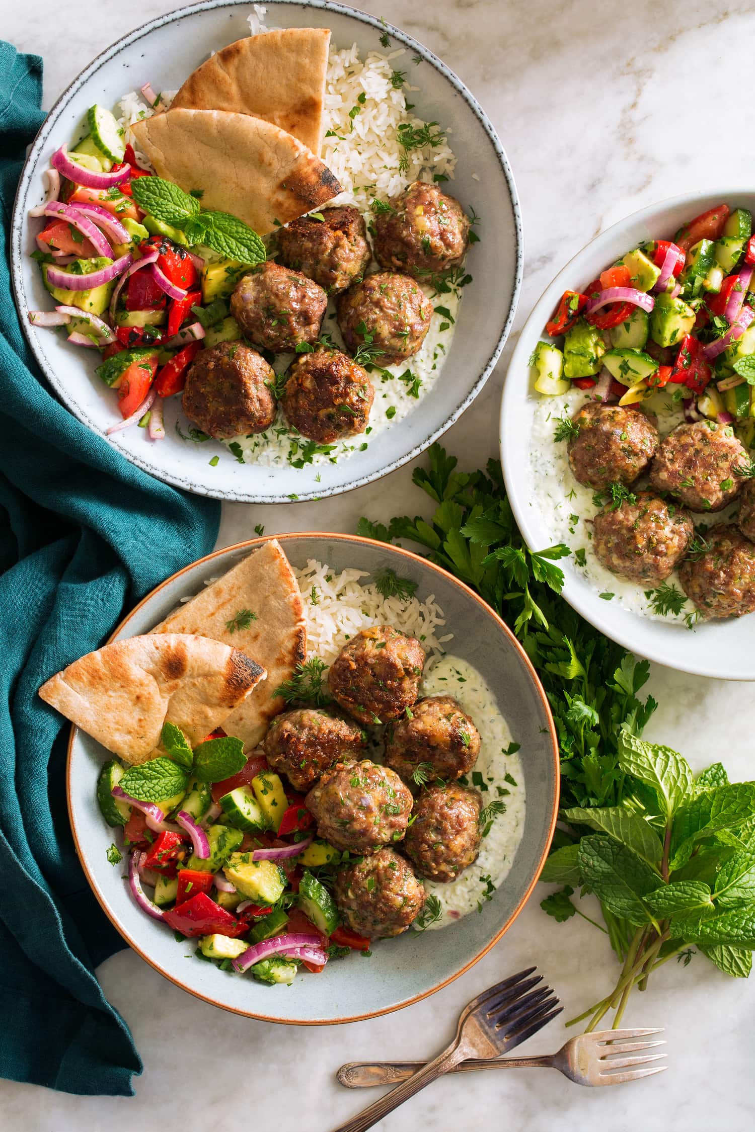 Three bowls of greek meatballs with pita and greek salad.