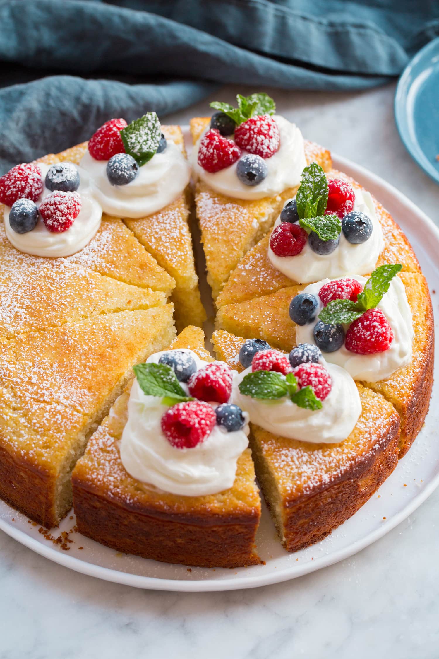 Whole yogurt cake sliced with cream and berries on top.