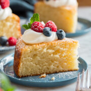 Slice of yogurt cake shown close up with yogurt and berries on top.