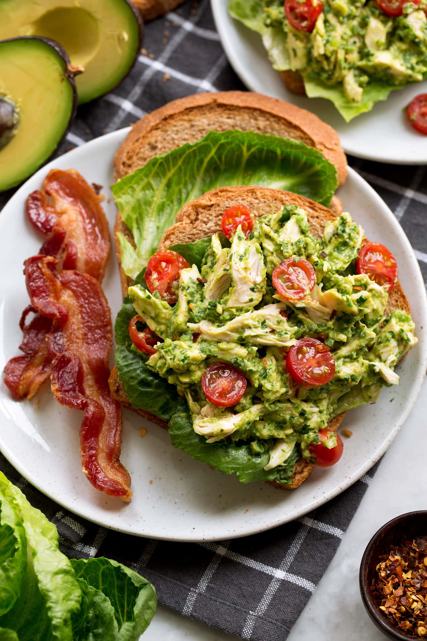 Avocado chicken salad shown on wheat bread with lettuce leaves and sliced grape tomatoes.