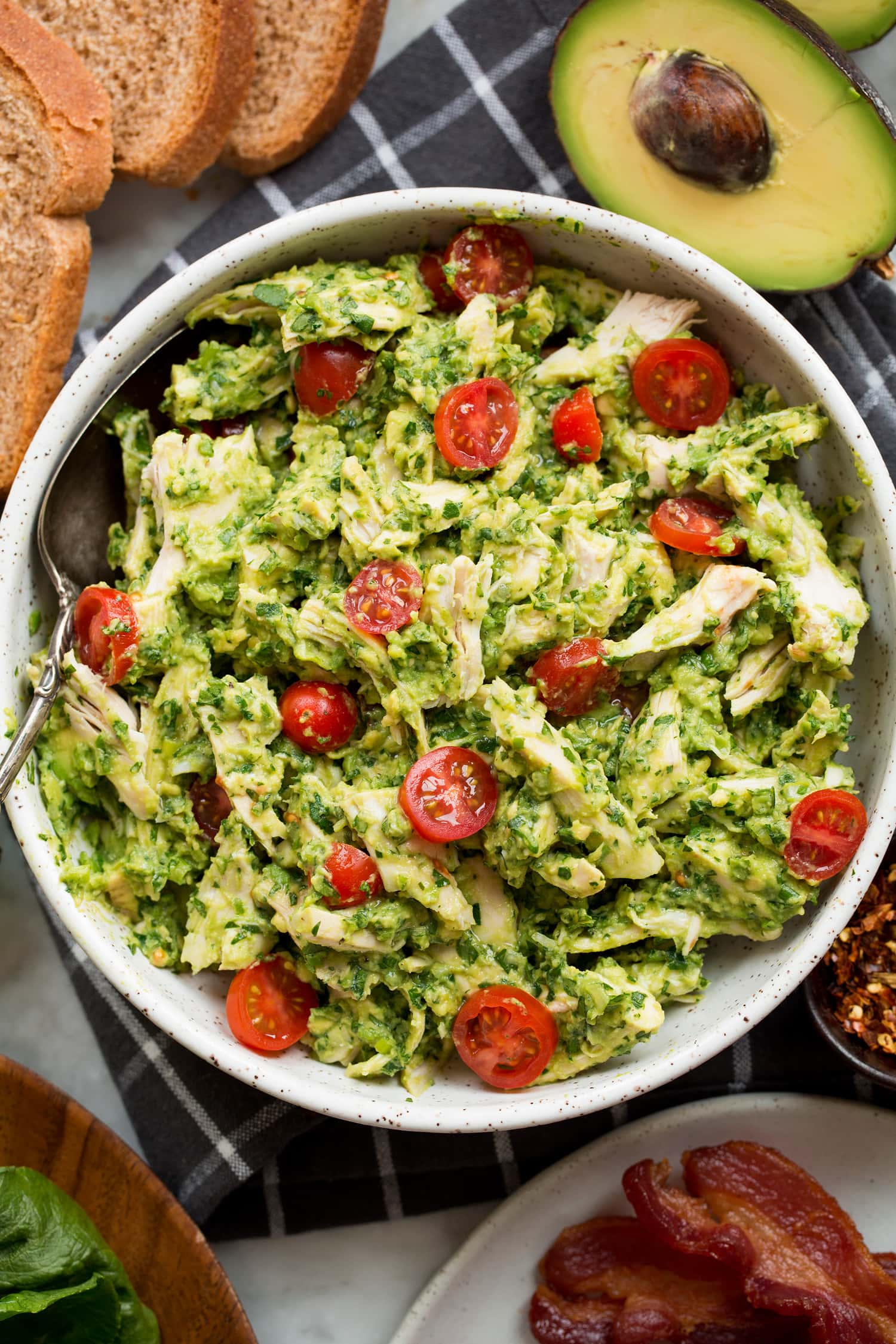 Avocado chicken salad with shredded chicken, mashed, avocado, tomato and bacon on the side.