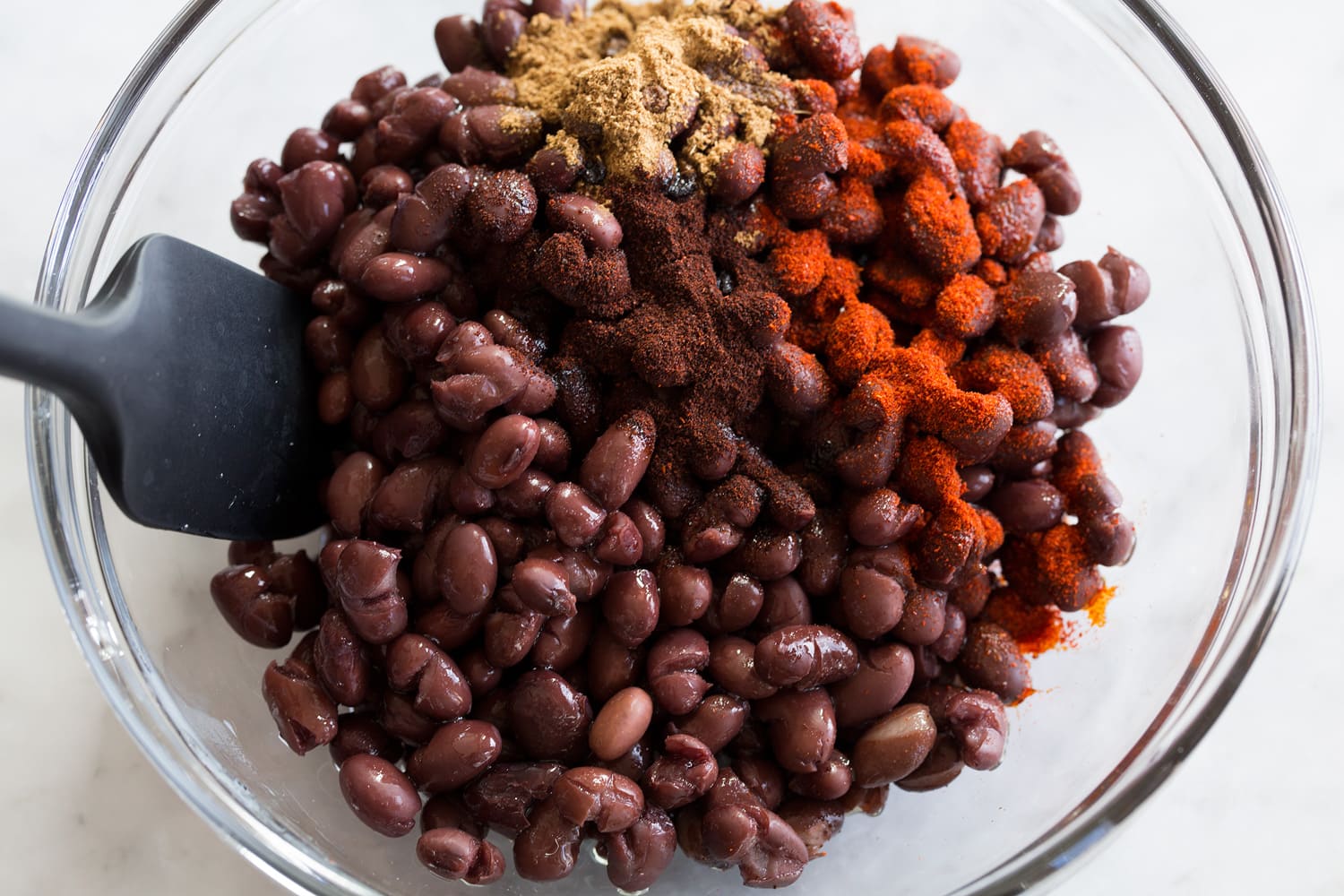 Black beans being tossed with spices in a mixing bowl.