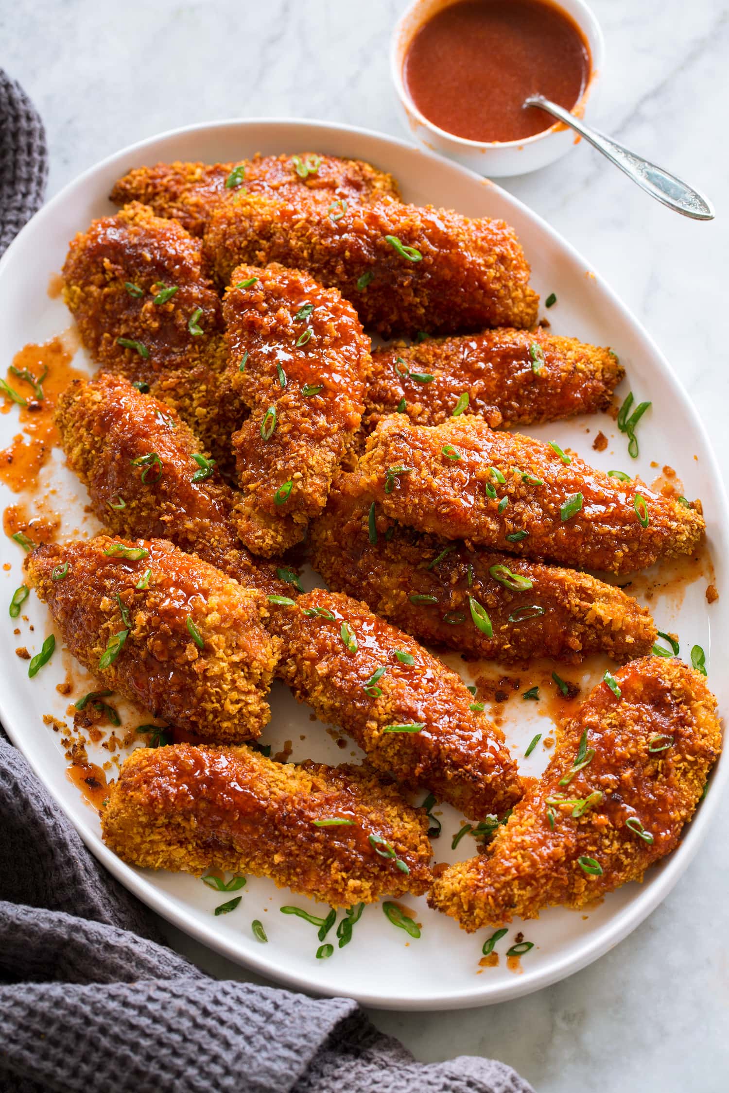 Hot honey chicken shown on a white oval platter garnished with green onions.