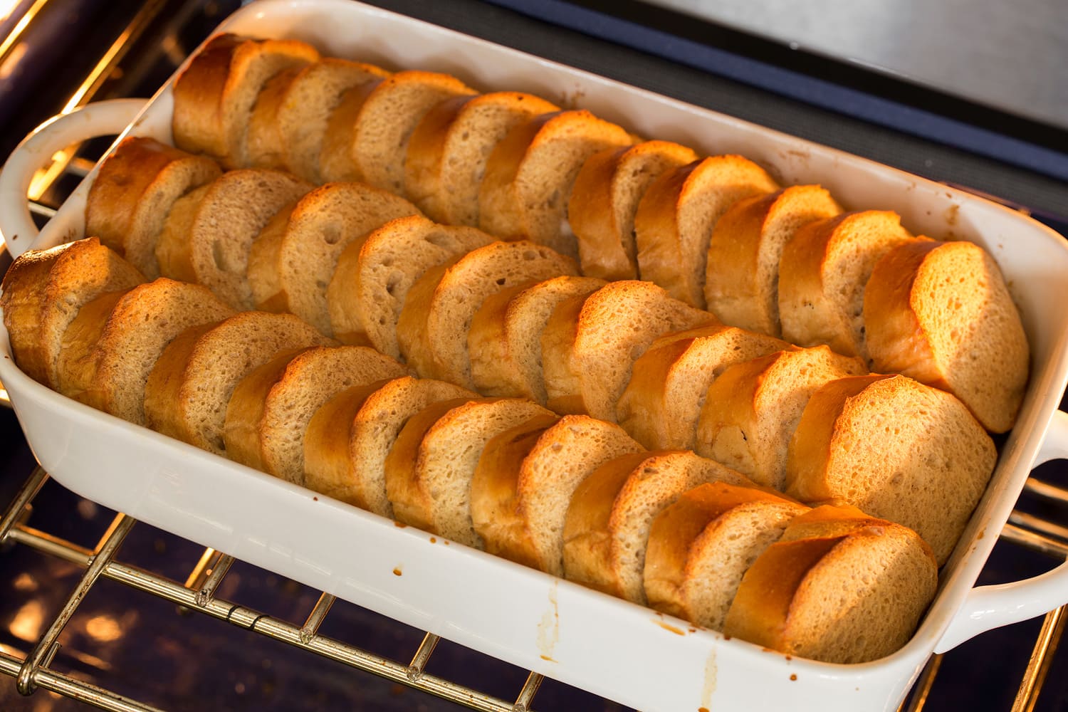 French toast in rows in baking dish shown baking in the oven.