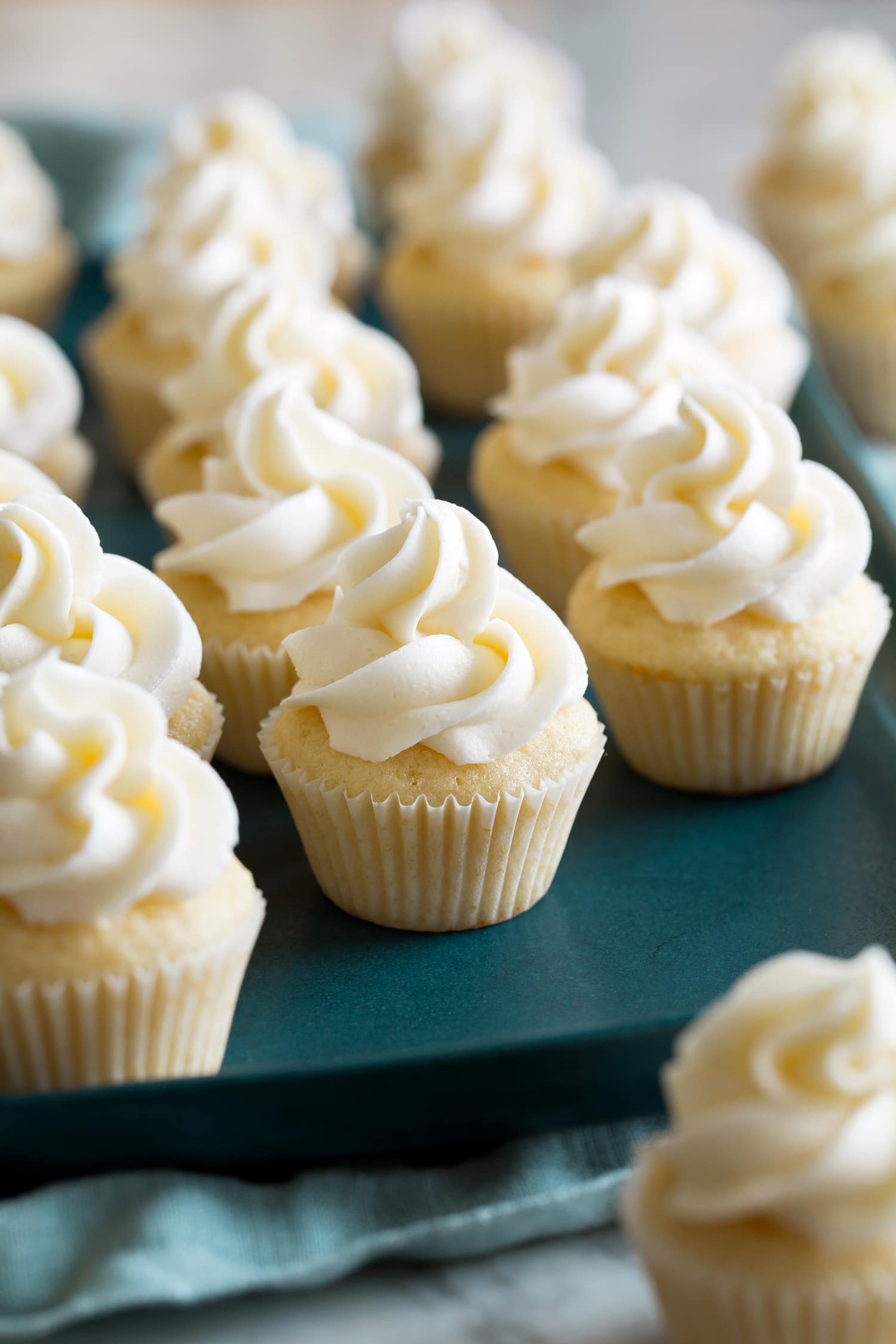 Mini vanilla cupcakes with buttercream frosting on a teal serving tray.