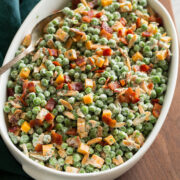 Pea salad with cheddar and bacon shown in an oval serving dish over a wooden board.