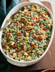 Pea salad with cheddar and bacon shown in an oval serving dish over a wooden board.