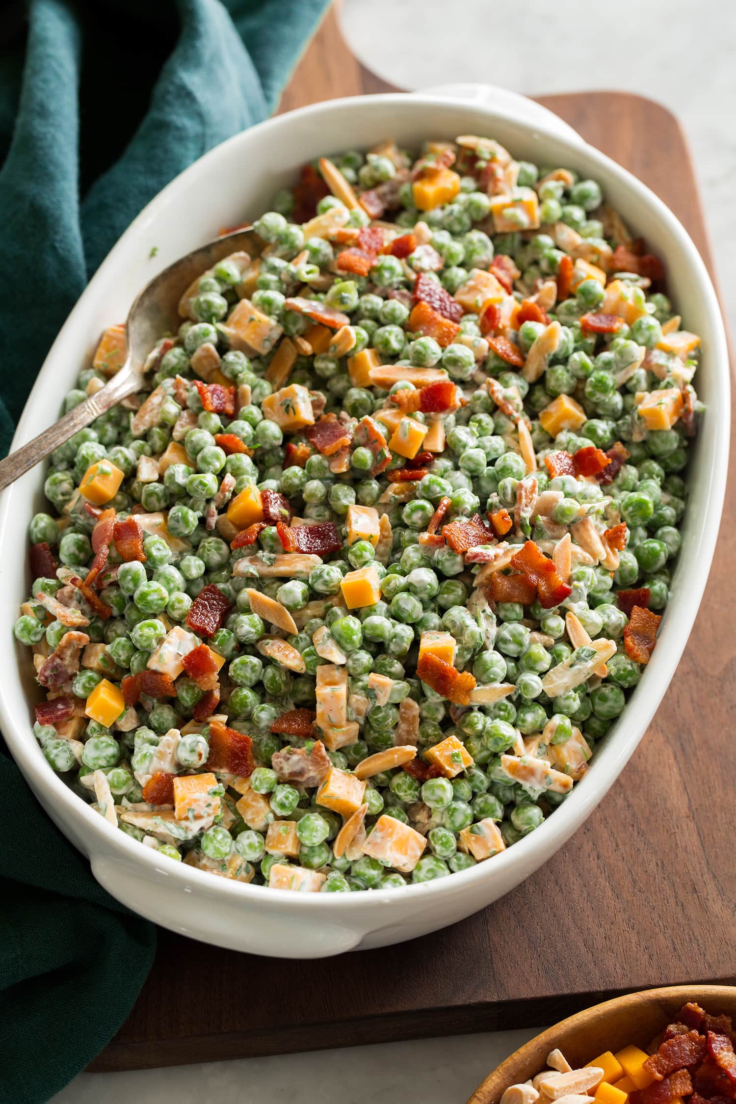 Pea salad with cheddar and bacon shown in an oval serving dish over a wooden board.