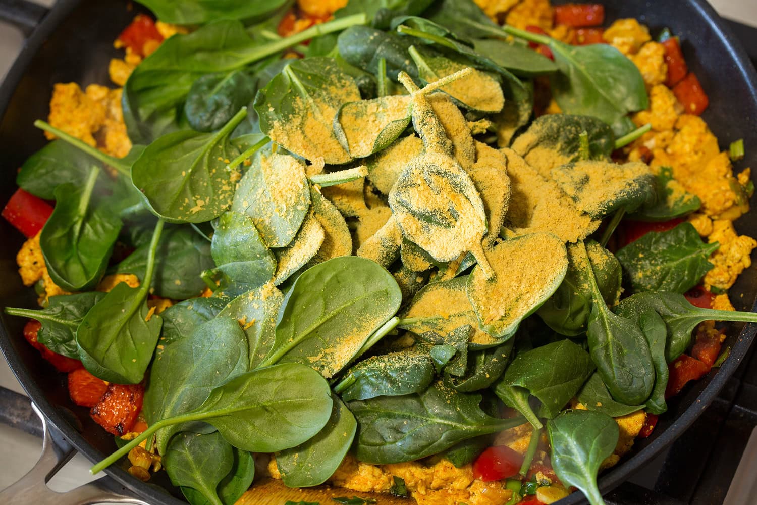 Adding spinach and nutritional yeast to skillet.